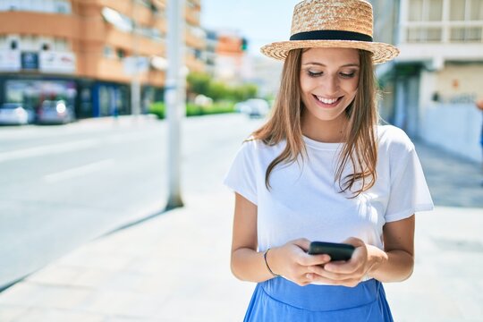Young blonde woman on vacation smiling happy using smartphone at street of city
