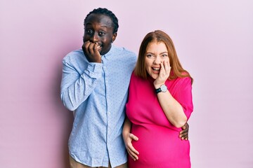 Young interracial couple expecting a baby, touching pregnant belly laughing and embarrassed giggle...