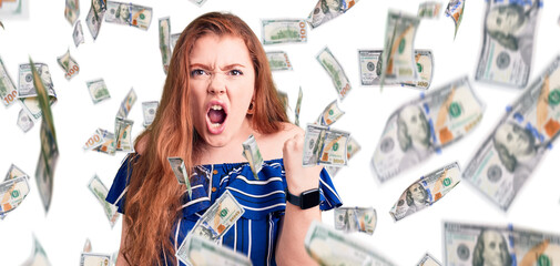 Young beautiful redhead woman wearing casual clothes angry and mad raising fist frustrated and...