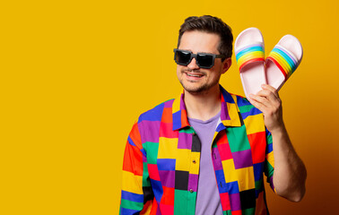 style guy in 90s shirt and pixel sunglasses holds flip flops on yellow background