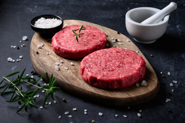 Raw ground beef meat burger steak cutlets with salt and rosemary on dark background