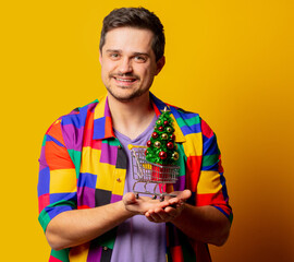 style guy in 90s shirt with Christmas tree in a cart on yellow background