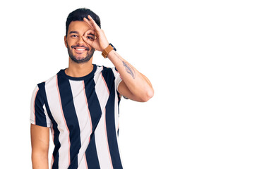 Fototapeta premium Young handsome hispanic man wearing striped tshirt doing ok gesture with hand smiling, eye looking through fingers with happy face.