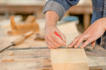 hand of a carpenter taking measurement of a wooden plank