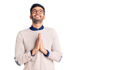 Young handsome hispanic man wearing elegant clothes and glasses begging and praying with hands...