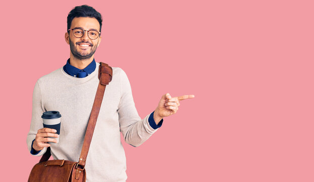 Young handsome hispanic man wearing leather bag and drinking take away coffee smiling happy pointing with hand and finger to the side