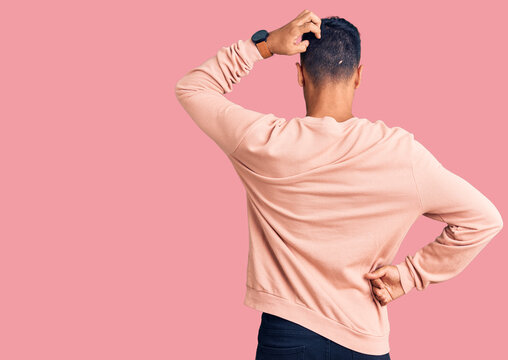 Young hispanic man wearing casual clothes backwards thinking about doubt with hand on head