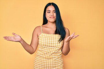 Young beautiful asian girl wearing casual clothes clueless and confused expression with arms and...