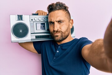 Handsome man with beard holding boombox, listening to music skeptic and nervous, frowning upset...