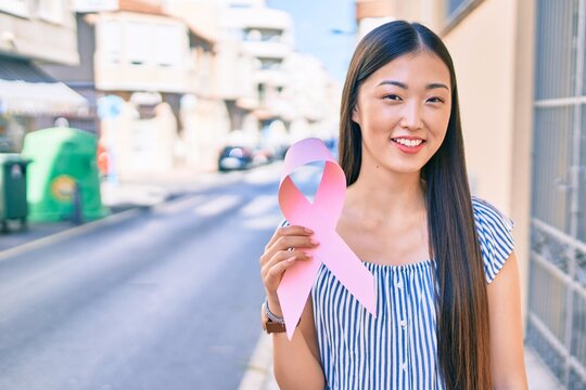 Young chinese woman smiling happy holding pink ribbon at street of city.