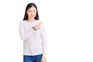 Young beautiful chinese woman wearing casual sweater pointing aside worried and nervous with forefinger, concerned and surprised expression