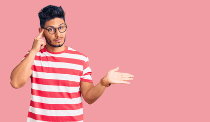 Handsome latin american young man wearing casual clothes and glasses confused and annoyed with open...