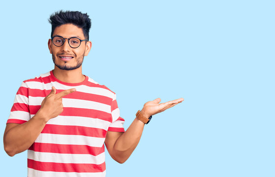 Handsome latin american young man wearing casual clothes and glasses amazed and smiling to the camera while presenting with hand and pointing with finger.