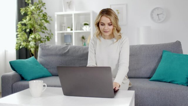 Adorable young female in domestic outfit sitting on cozy sofa and typing on modern laptop. Relaxing tim at home. Technology concept.