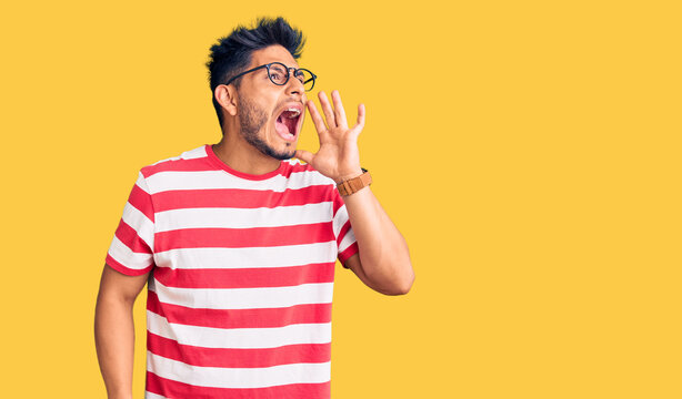 Handsome latin american young man wearing casual clothes and glasses shouting and screaming loud to side with hand on mouth. communication concept.