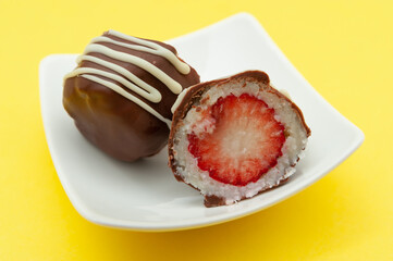 Chocolate egg (Easter egg) coconut stuffed with strawberry sliced in half on a plate. Isolated on yellow background. Close-up. Horizontal shot.