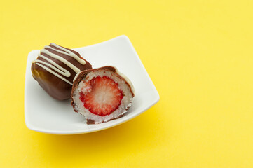 Chocolate egg (Easter egg) coconut stuffed with strawberry sliced in half on a plate. Isolated on yellow background. Copy space. Horizontal shot.