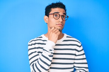 Young handsome hispanic man wearing casual sweater and glasses serious face thinking about question...