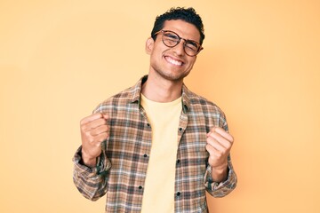 Young handsome hispanic man wearing casual clothes and glasses very happy and excited doing winner...