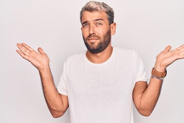 Young handsome blond man wearing casual t-shirt standing over isolated white background clueless...