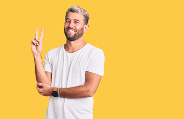 Young handsome blond man wearing casual t-shirt with a big smile on face, pointing with hand and finger to the side looking at the camera.