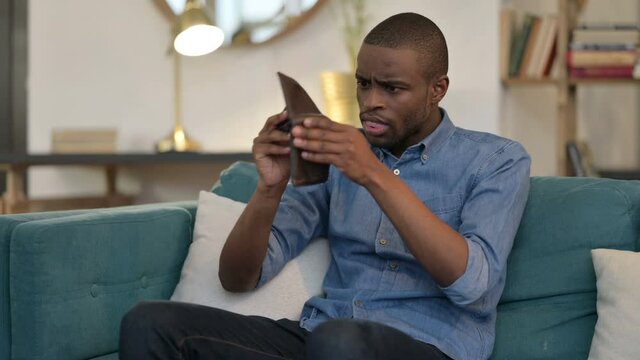 Broke Young African Man Checking Empty Wallet on Sofa 