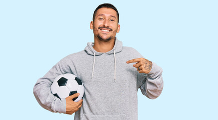 Handsome man with tattoos holding soccer ball pointing finger to one self smiling happy and proud