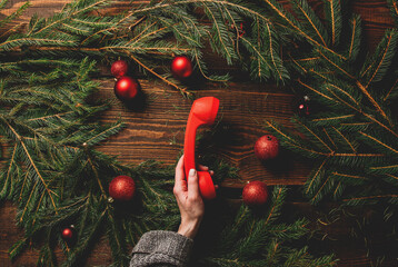 Female hands hold red handset next to Christmas decoration