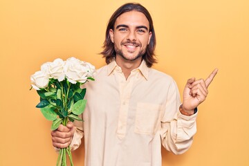 Young handsome man holding flowers smiling happy pointing with hand and finger to the side