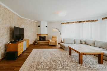 Contemporary interior of living room in modern flat. Soft leather chair near fireplace. Huge TV on chest of drawers. Wooden table. Cozy sofa.