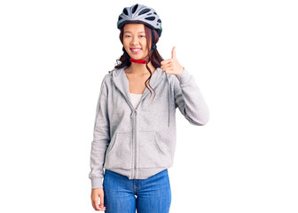 Young beautiful chinese girl wearing bike helmet smiling happy and positive, thumb up doing excellent and approval sign
