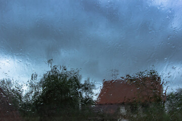 Drops on glass in rainy day.Rain outside window in the countryside. Texture of raindrops, wet glass.Rainy window background.View through the window with stormy sky. Staying at home. Weather changes.