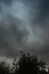 Drops on glass in rainy day.Rain outside window in the countryside. Texture of raindrops, wet glass.Rainy window background.View through the window with stormy sky. Staying at home. Weather changes.