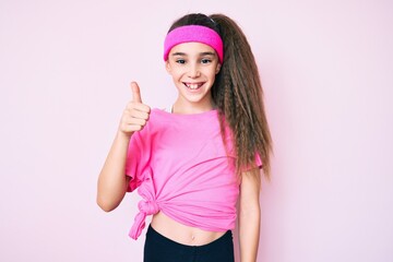 Obraz na płótnie Canvas Cute hispanic child girl wearing sportswear smiling happy and positive, thumb up doing excellent and approval sign