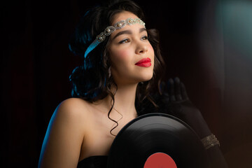 Old-fashioned woman dressed in style of art deco holding vinyl record on dark background. Roaring...