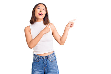 Young beautiful chinese girl wearing casual clothes smiling and looking at the camera pointing with two hands and fingers to the side.