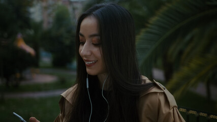 Pretty young smiling woman with her phone and headset listens to music and happily dances on foot,...