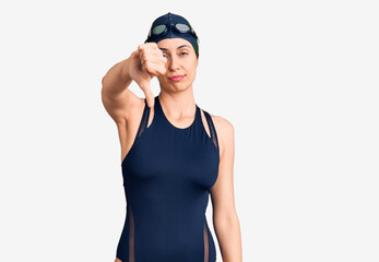 Young beautiful hispanic woman wearing swimwear and swimmer glasses looking unhappy and angry showing rejection and negative with thumbs down gesture. bad expression.