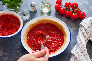 Step-by-step preparation of an Italian spiral pie with zucchini, carrots, step 2 - filling with tomato sauce with herbs, female hands spread the filling into a baking dish, horizontal