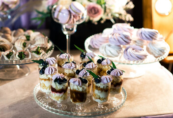 A wedding cake decorated with flowers stands on a festive table with desserts, tartlets and cupcakes.