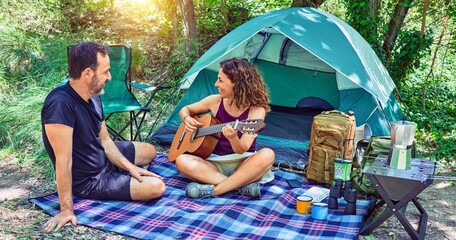 Middle age couple  of hiker smiling happy camping at the forest. Sitting on the floor singing song playing classical guitar