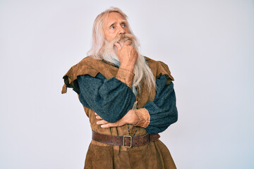 Old senior man with grey hair and long beard wearing viking traditional costume with hand on chin thinking about question, pensive expression. smiling with thoughtful face. doubt concept.