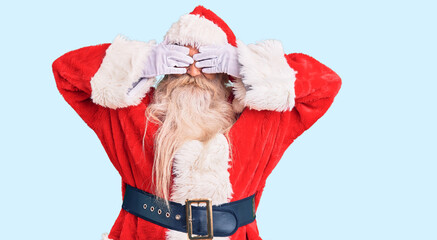 Old senior man with grey hair and long beard wearing traditional santa claus costume covering eyes with hands smiling cheerful and funny. blind concept.