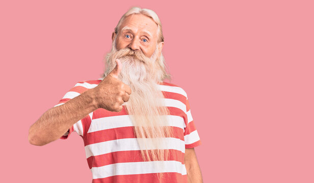 Old senior man with grey hair and long beard wearing striped tshirt doing happy thumbs up gesture with hand. approving expression looking at the camera showing success.