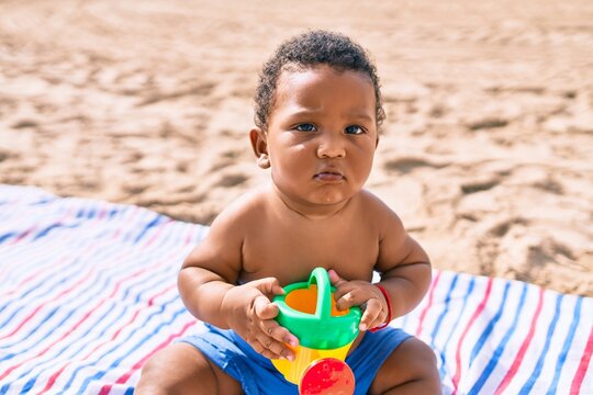 Adorable african american toddler playing with toys sitting on the sand at the beach.