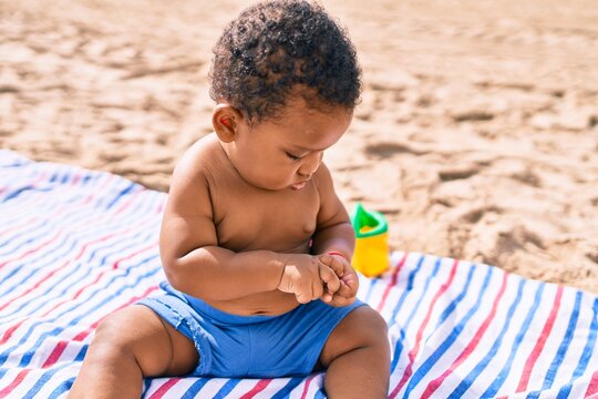 Adorable african american toddler playing with toys sitting on the sand at the beach.