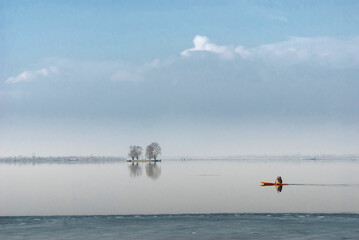 A boatman in a small red wooden boat on a lake partially covered with ice.