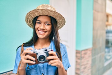 Young latin tourist girl on vacation smiling happy using vintage camera at the city.