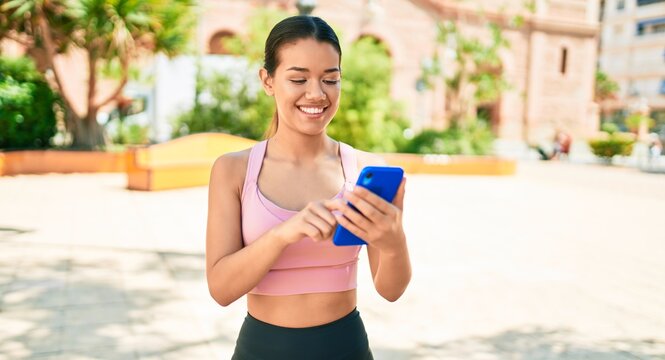 Young beautiful hispanic sporty woman wearing fitness outfit smiling happy and natural texting using smartphone at the town