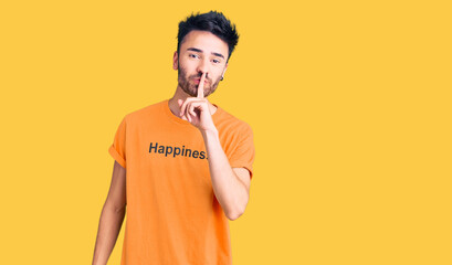 Young hispanic man wearing t shirt with happiness word message asking to be quiet with finger on lips. silence and secret concept.